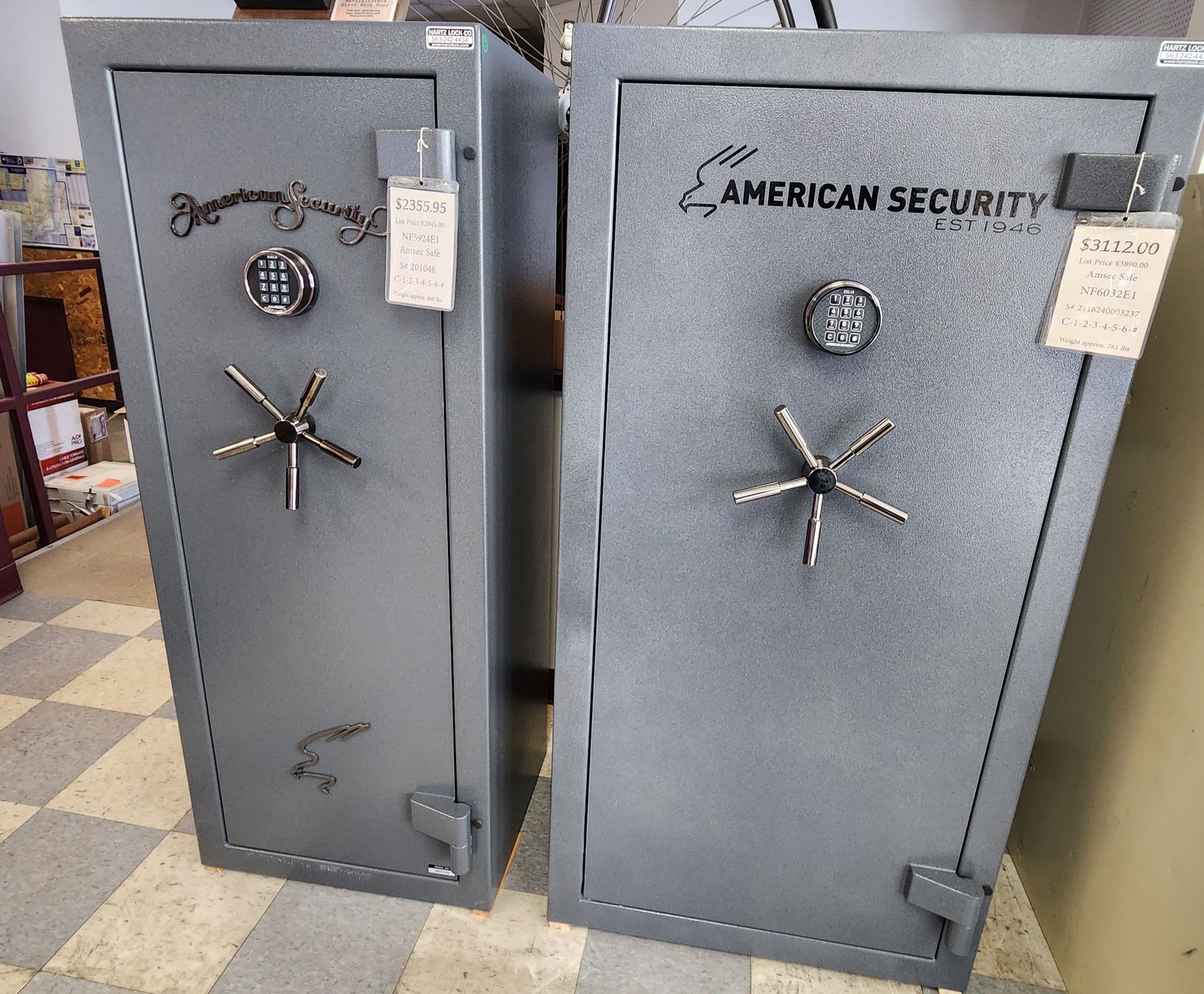 Two gray American Security gun safes with digital keypads and five-spoke handles standing side-by-side on a tiled floor.
