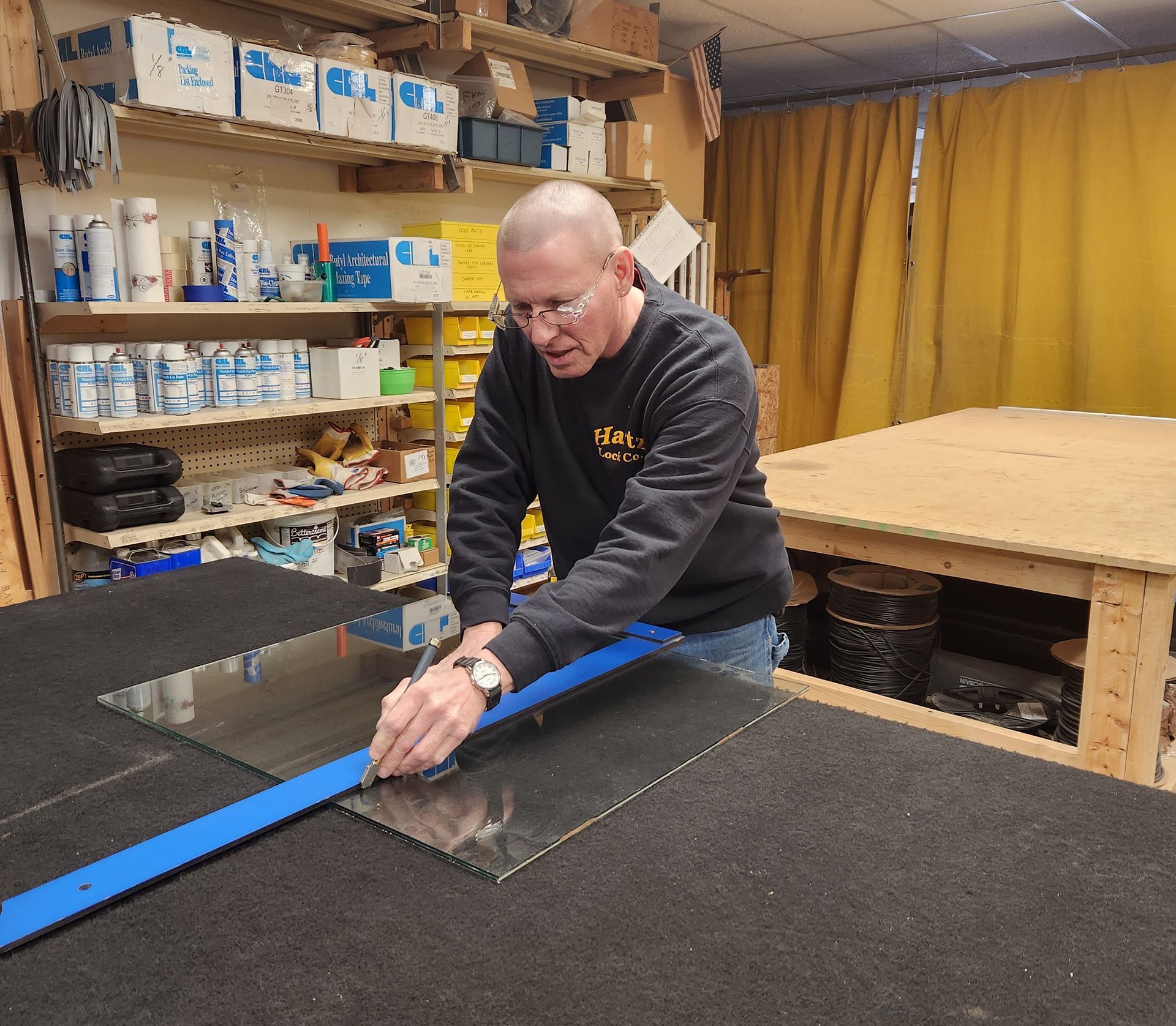 Man cutting glass with a ruler in a workshop, wearing a black sweater.