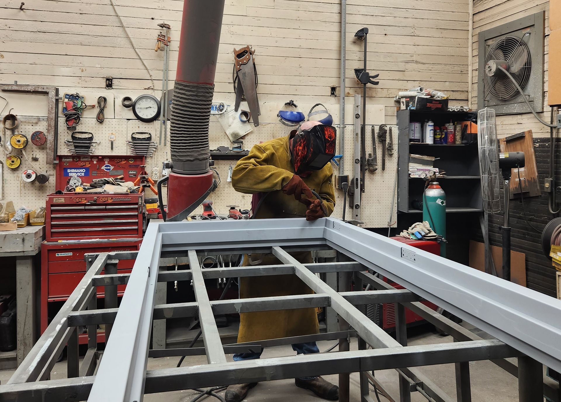 Welder in protective gear working on a metal frame in a workshop.