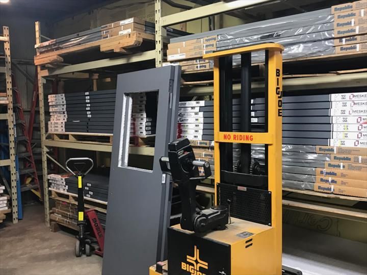 Warehouse interior with a gray door, yellow forklift, and stacked shelves with building supplies.