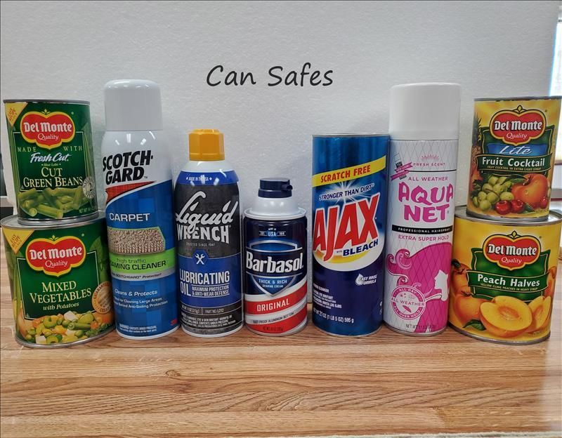 Assorted can safes disguised as canned goods, household sprays, and shaving cream, lined up on a wooden surface.