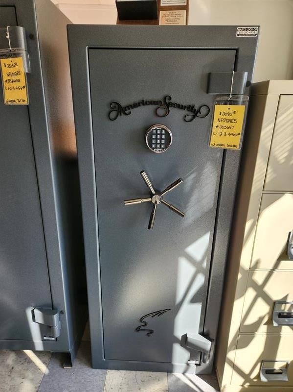 Gray security safe with a digital keypad, handle, and decorative scrollwork in a retail setting.