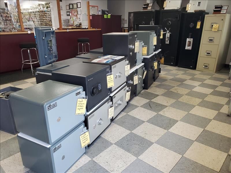 A store displays various safes on the floor, ranging in size and color, with a checkered tile floor.