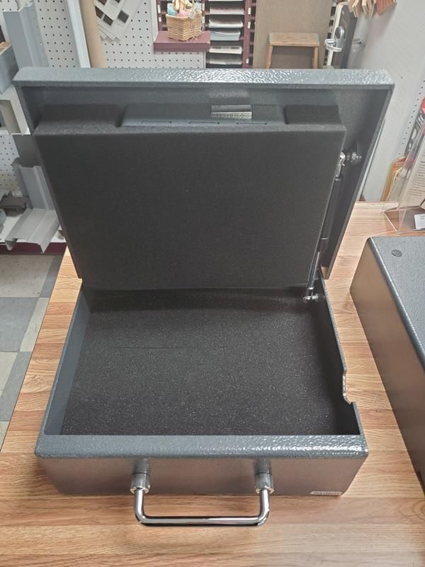 Open gray metal cash box with handle, foam padding visible inside on a wooden surface.