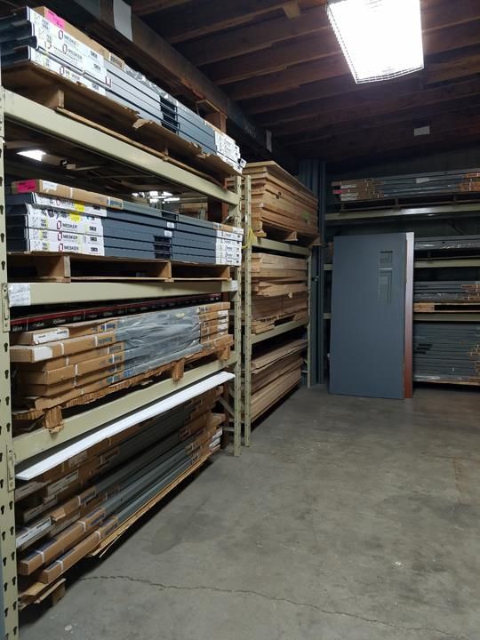 Warehouse shelving stacked with various building materials. A gray safe stands nearby.