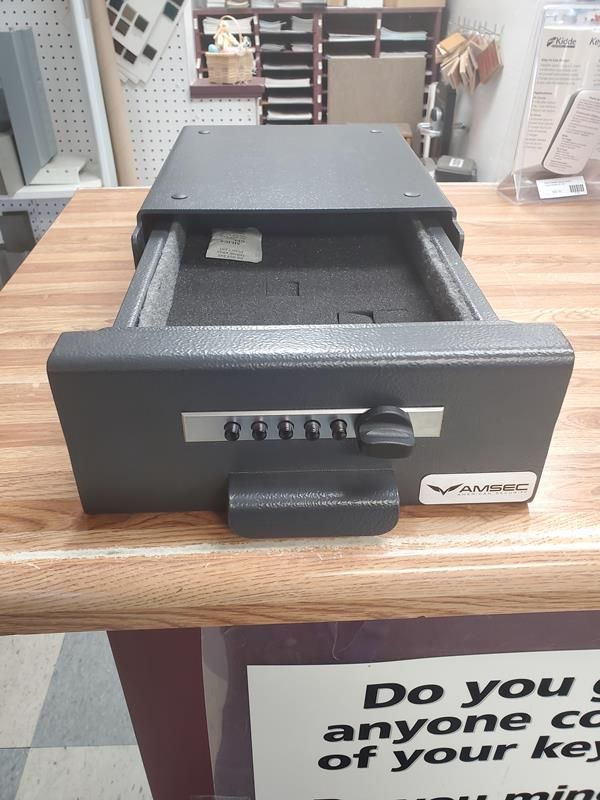 A black V-Line drawer safe with a combination lock, open on a wood-grain surface.