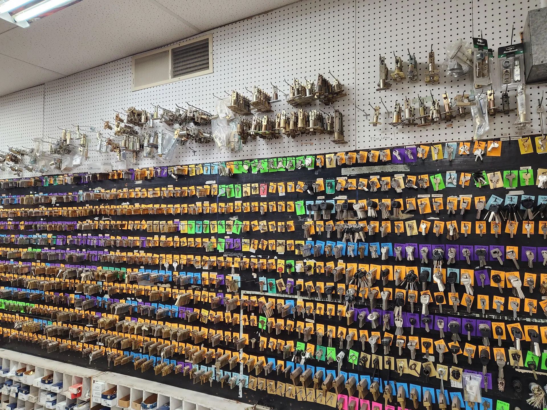 Wall of various keys for sale in a hardware store; many colors, organized on pegboard.
