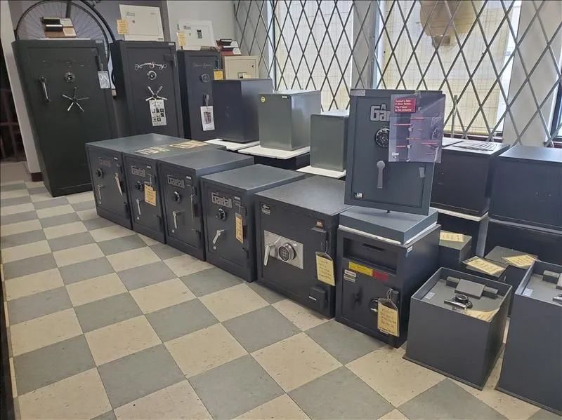 A room displays a variety of gray safes on checkered floor, near windows.