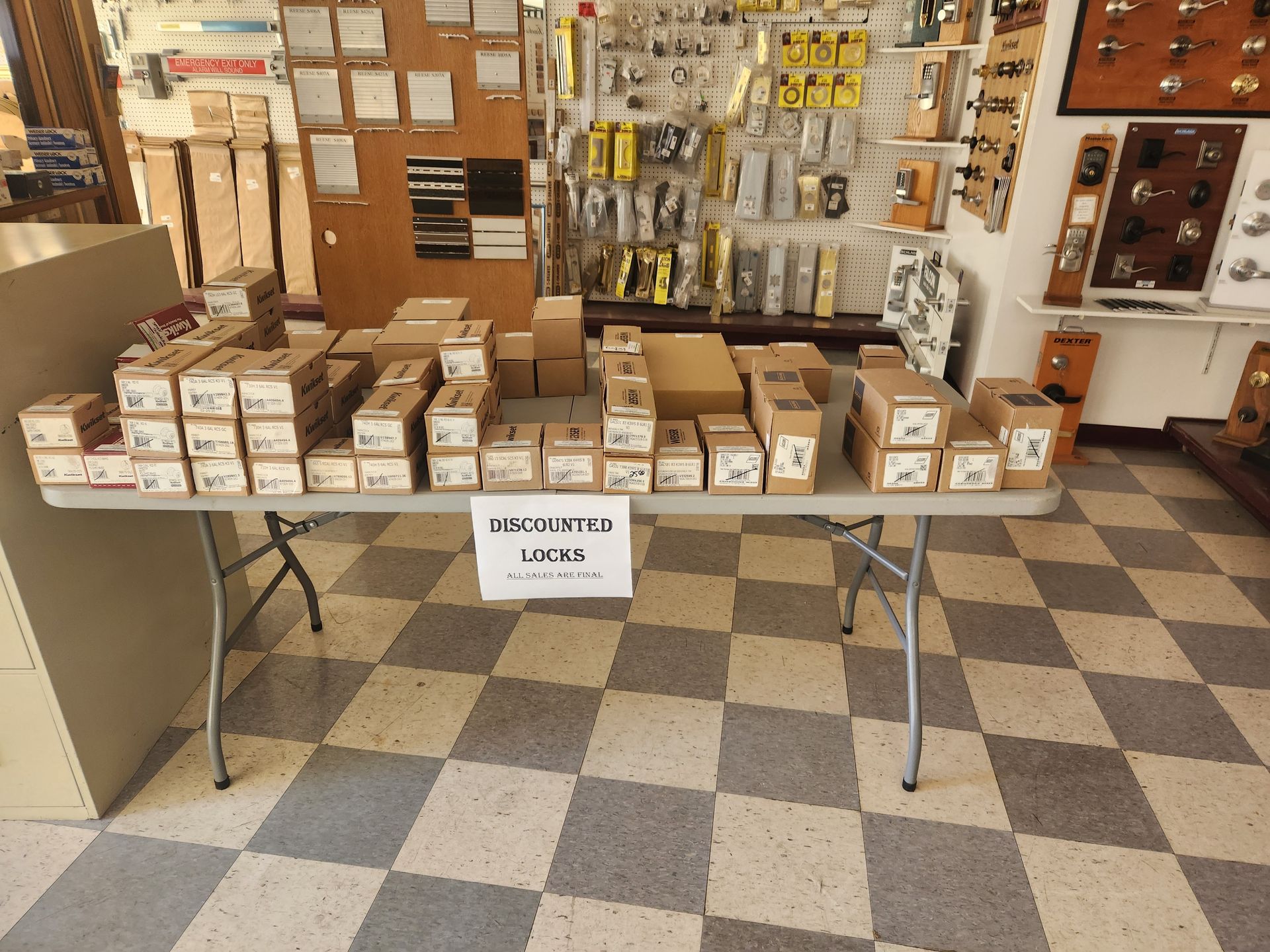 Table displaying various hardware boxes in a store, checkered floor, tools on shelves in the background.