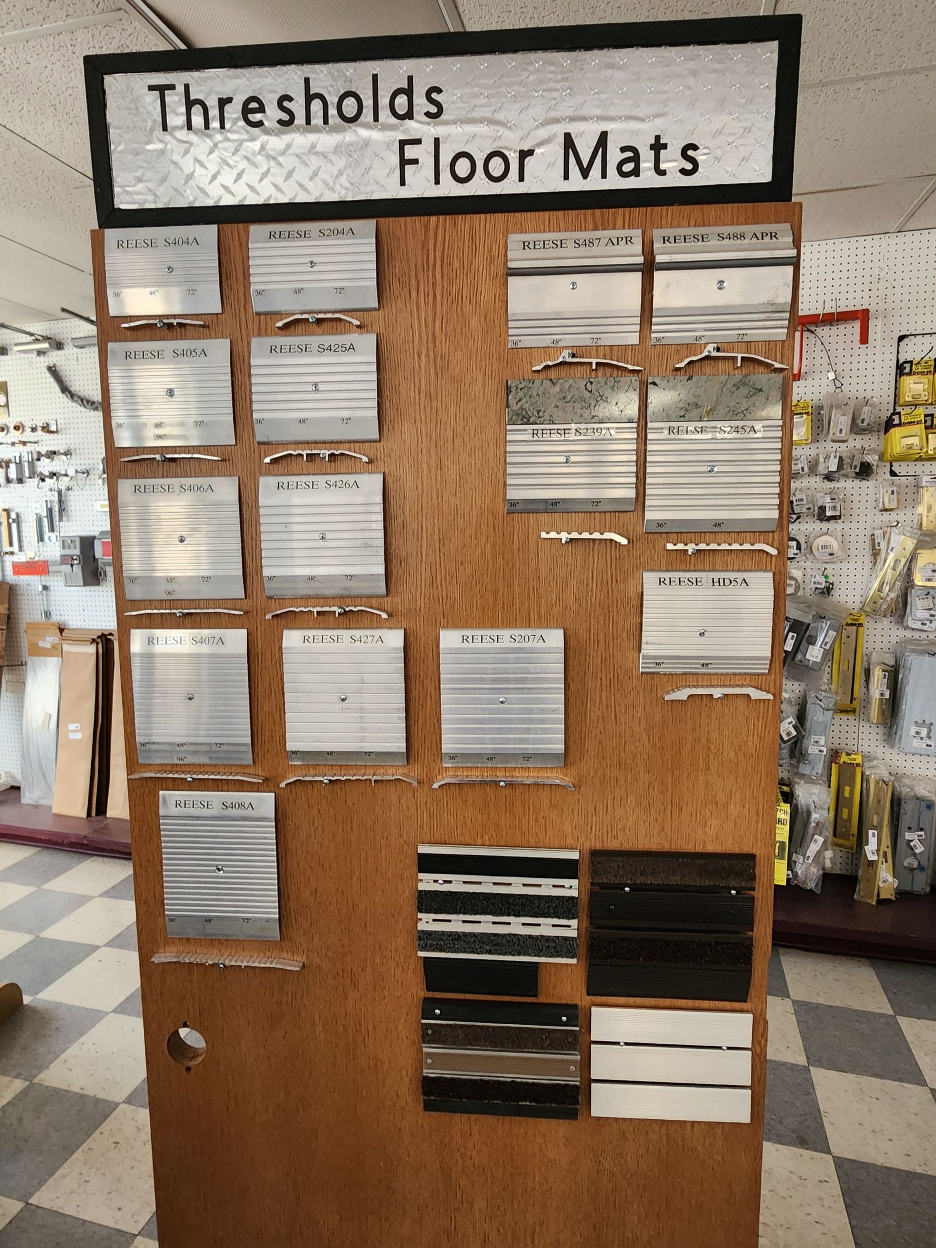 Display board of threshold and floor mat samples in a hardware store, various metal and wood textures.