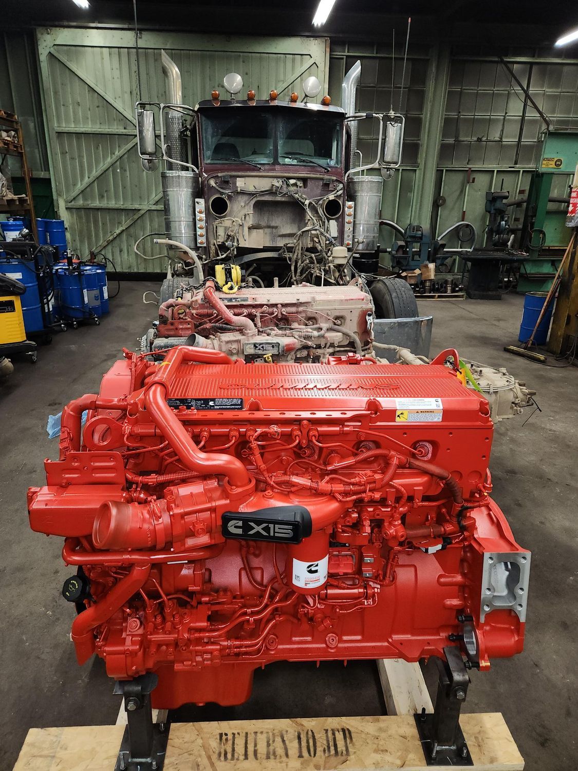 Red Cummins engine ready for installation in a semi-truck cab in a workshop.