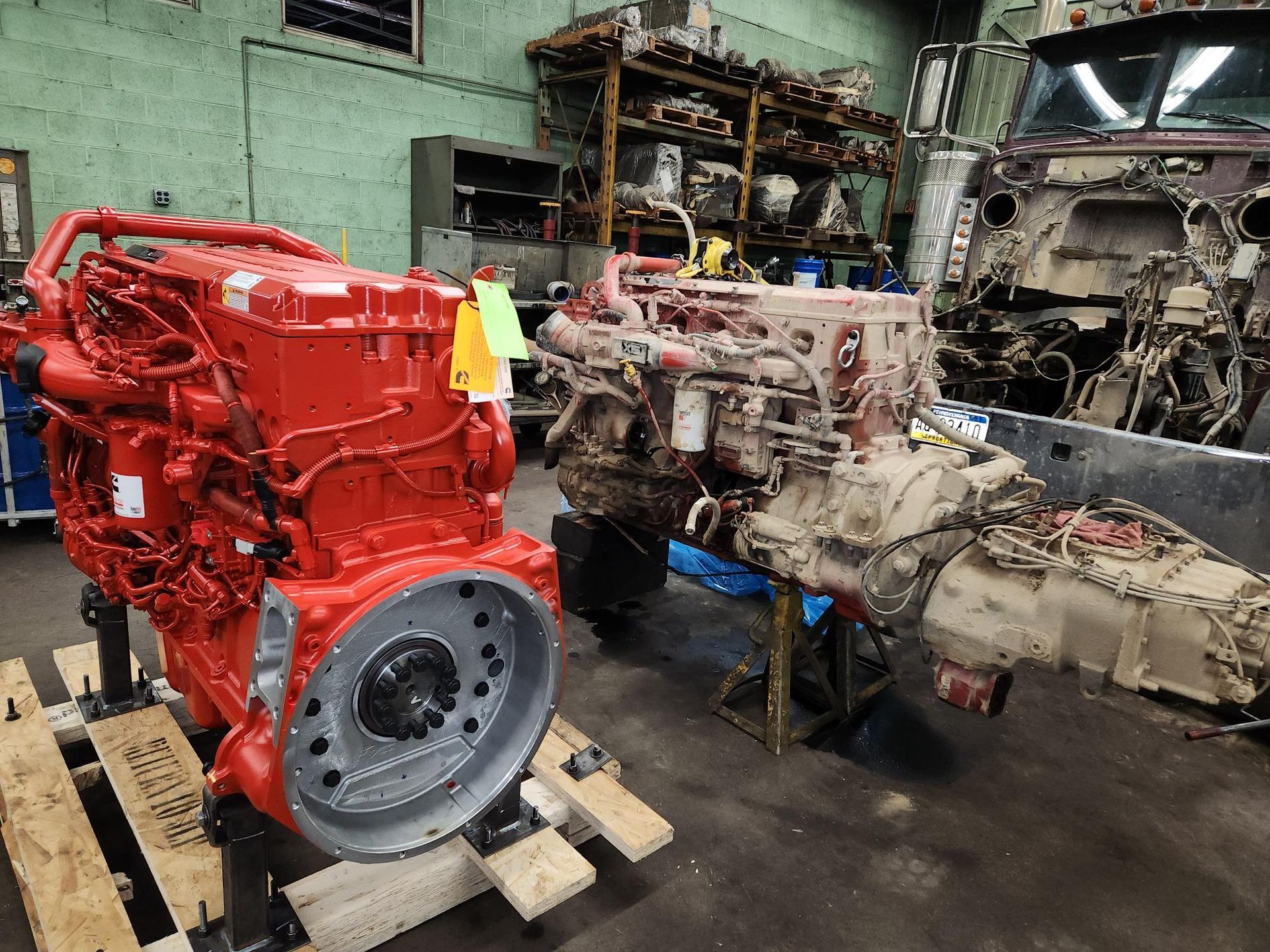 Two red and dirty truck engines in a workshop, one new and one older.