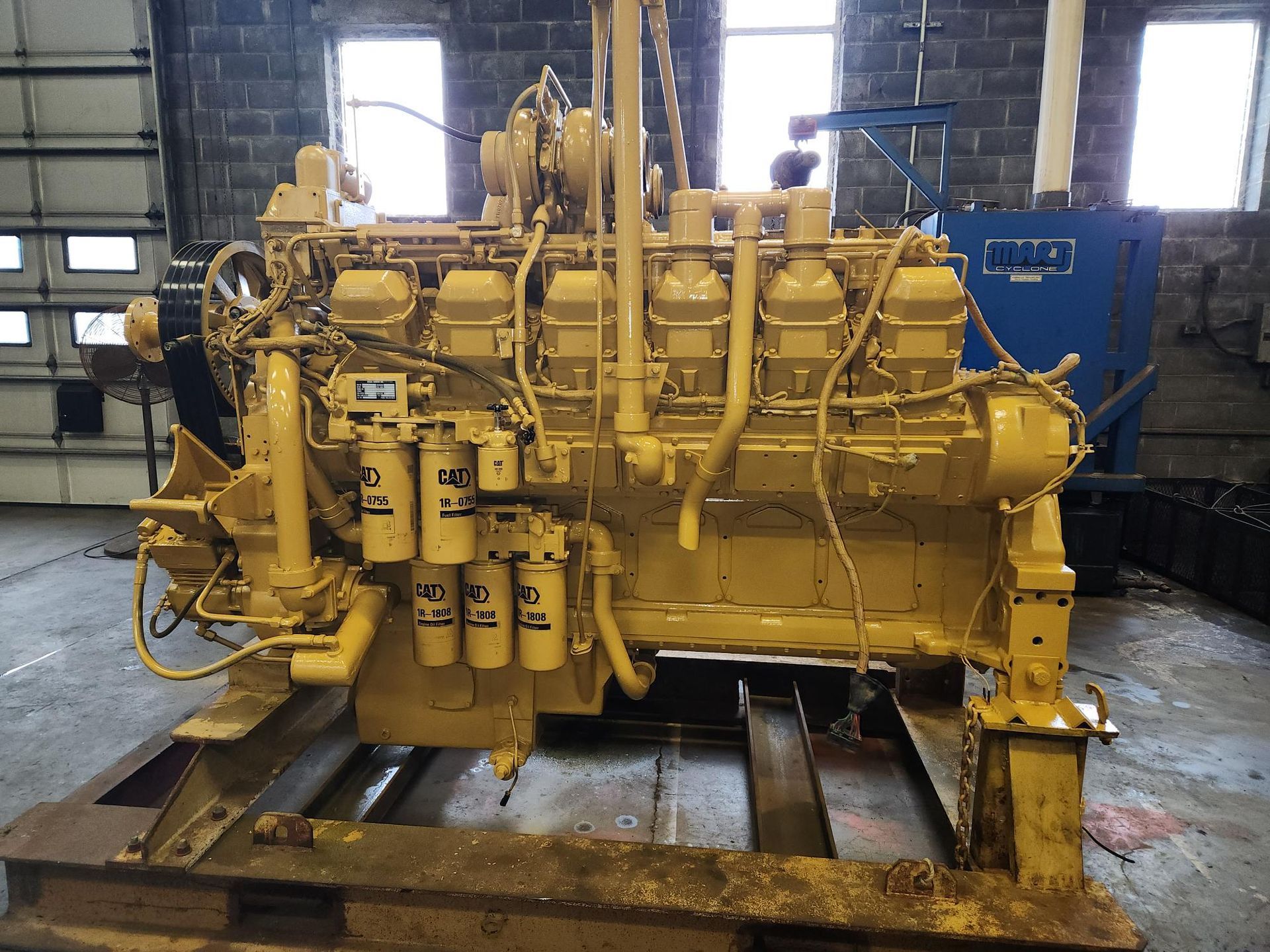 Yellow industrial diesel engine mounted on a metal stand in a workshop.