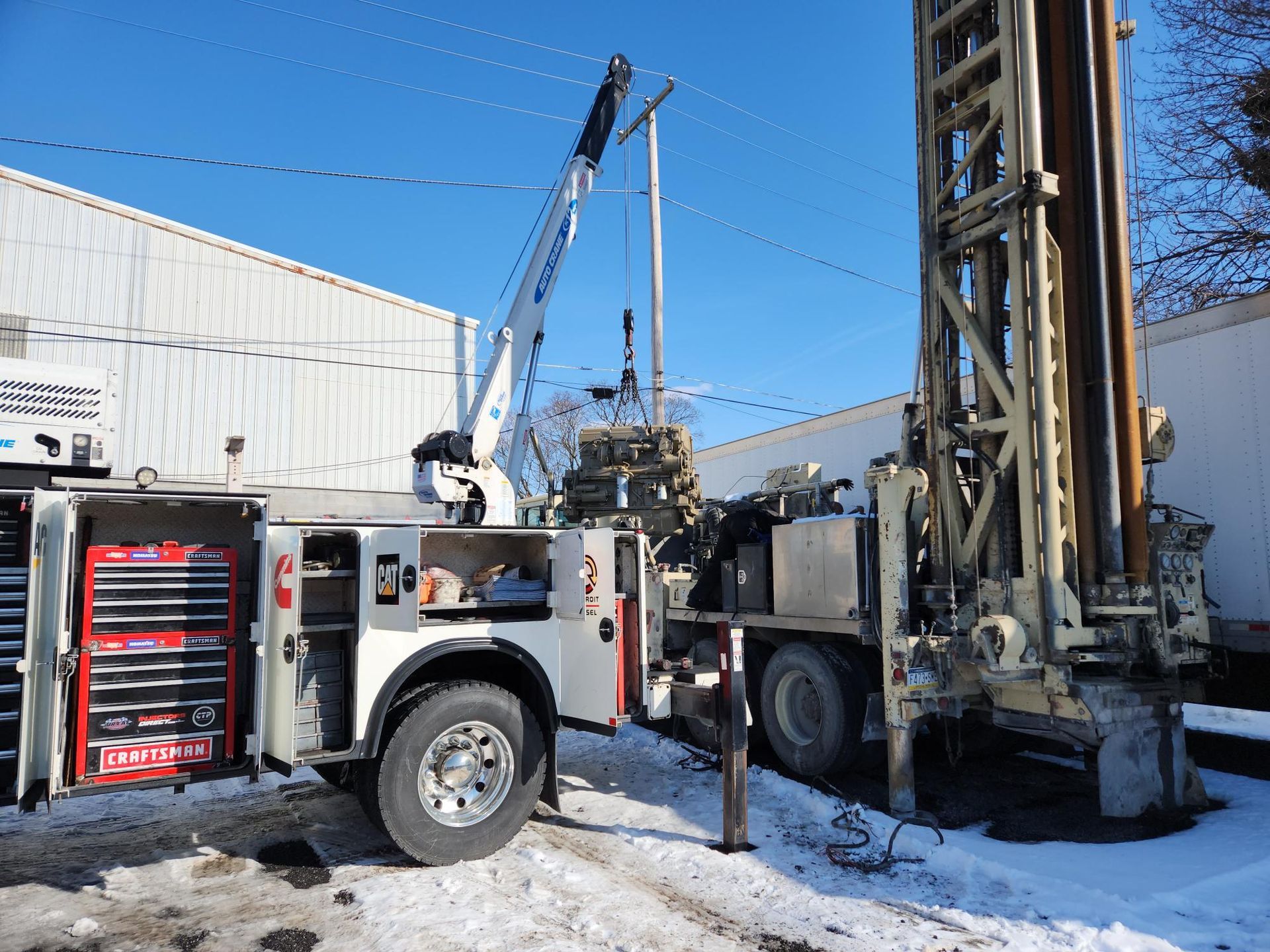 Drilling rig truck with open toolbox and extended crane arm in snowy environment.