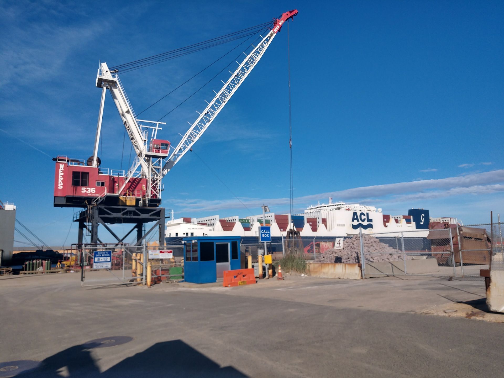Harbor scene with a large red and white crane, ACL ship, blue sky.