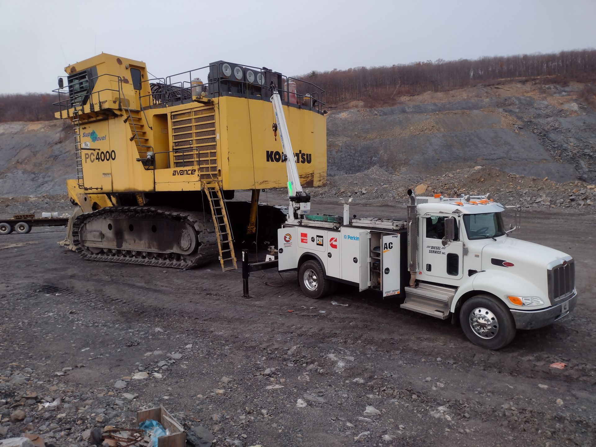 A large yellow mining machine being serviced by a white service truck in a quarry.