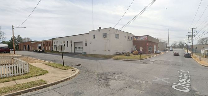 Street scene with light-colored buildings, a white fence, and a street sign that says