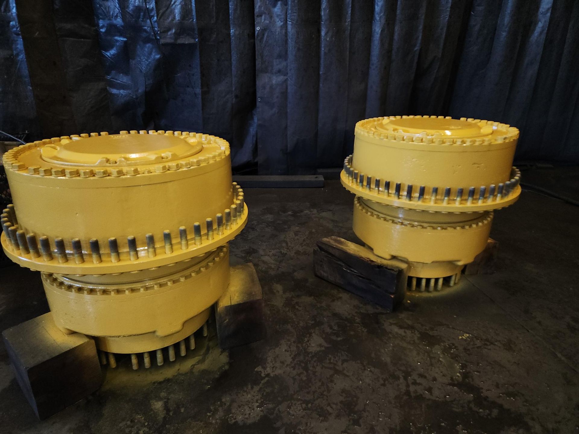 Two yellow industrial machine components with circular gear-like edges, resting on blocks against a dark backdrop.