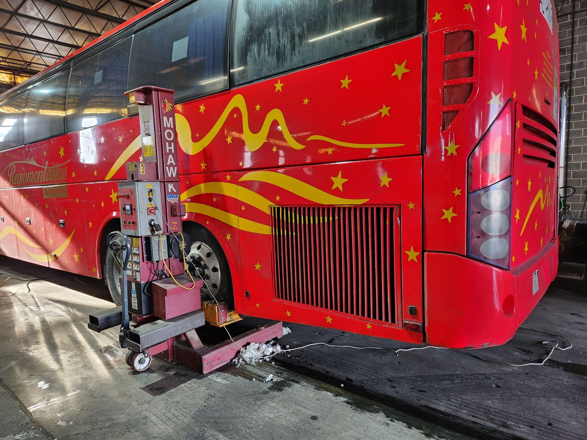 Red bus with star and wave decorations being serviced by a mobile lift in a garage.
