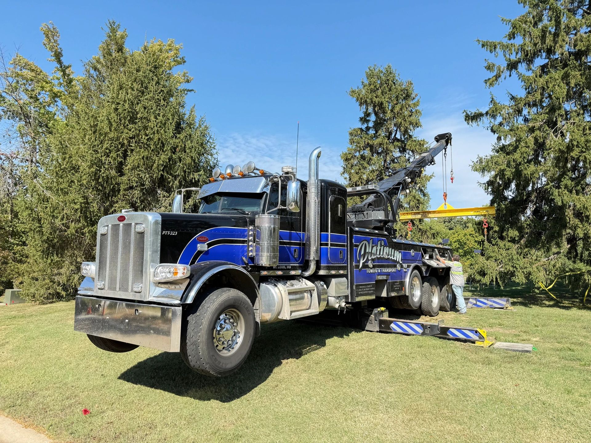 Blue and black tow truck parked on grass under a clear, blue sky.
