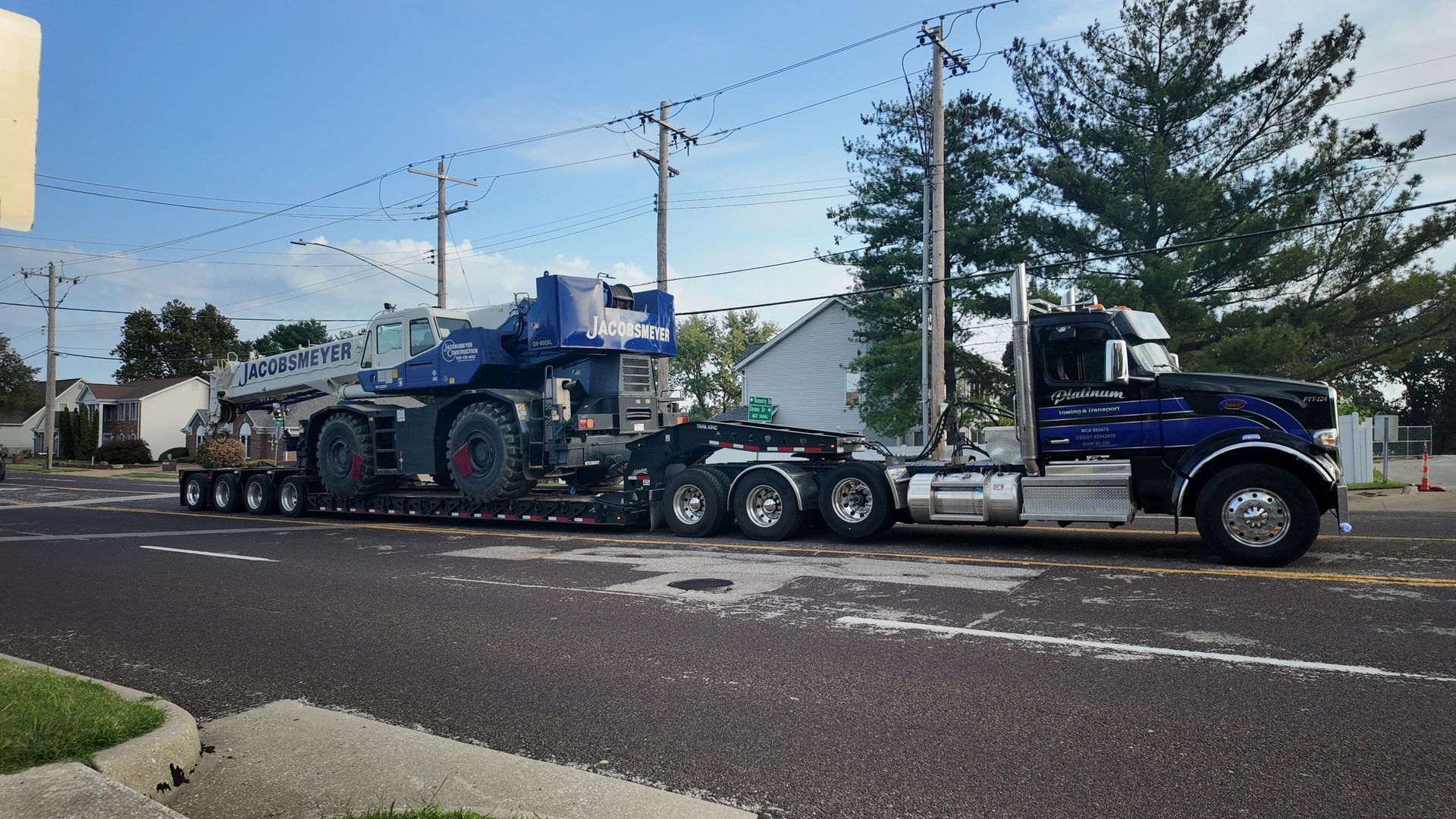 Semi-truck transporting a large crane on a lowboy trailer on a street.