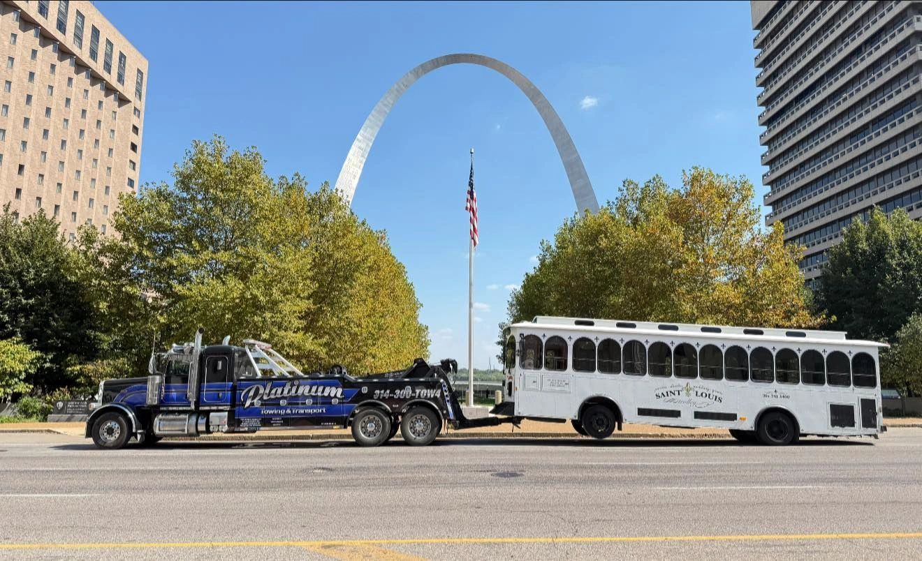 Tow truck hauling trolley, Gateway Arch in background, St. Louis. Sunny day.