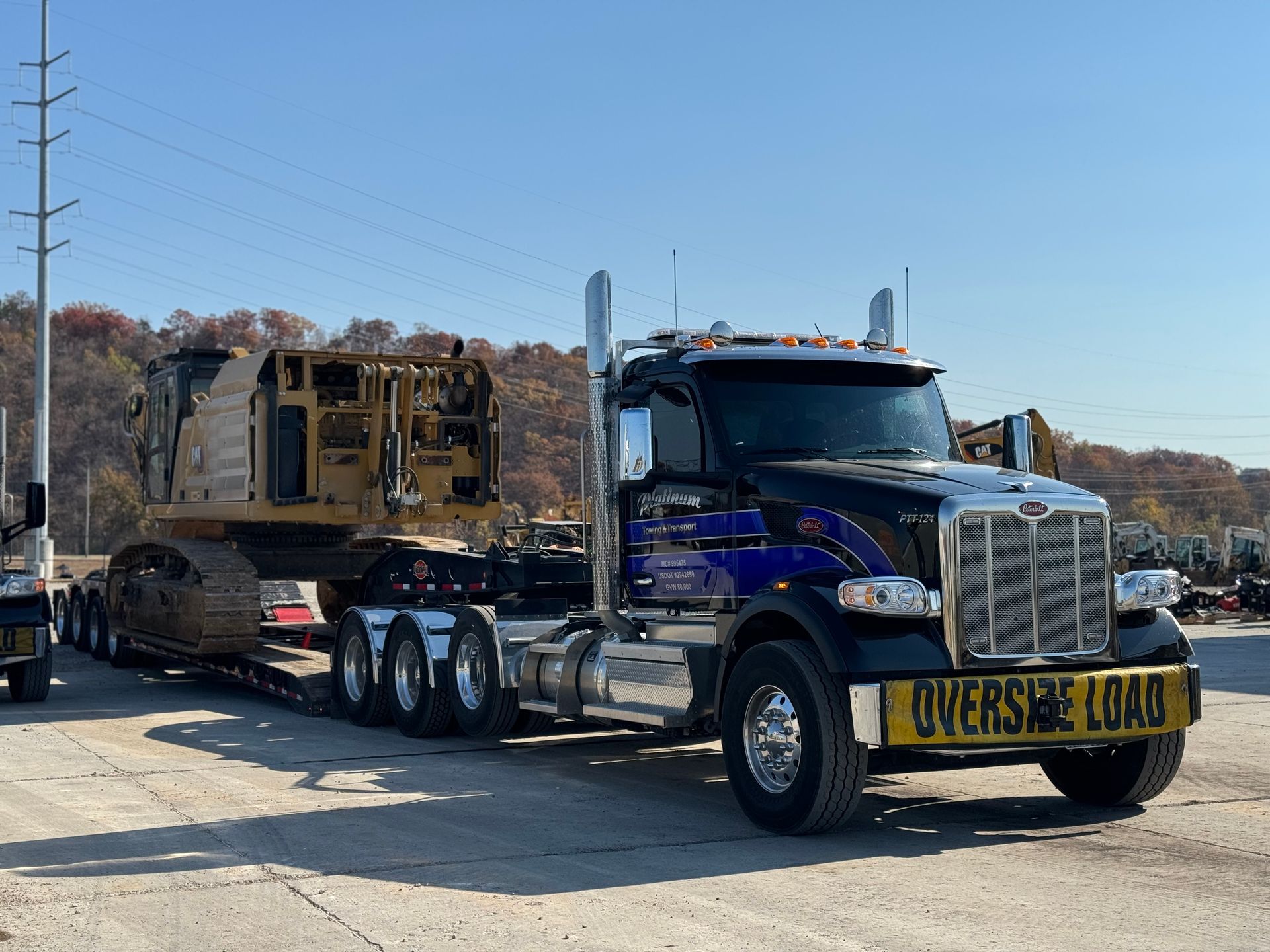 Black semi-truck hauling a yellow construction vehicle on a lowboy trailer; 
