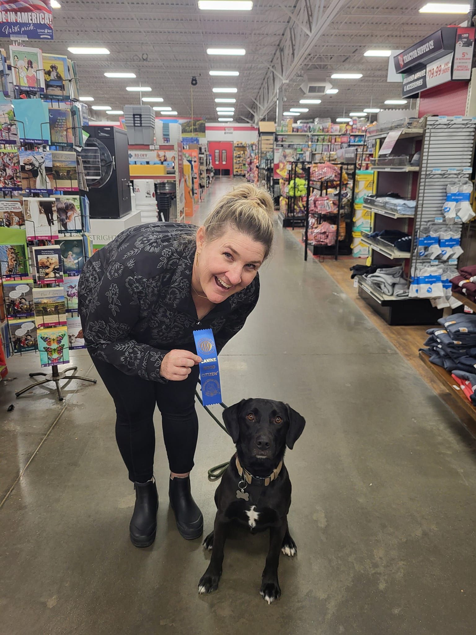A woman is standing next to a black dog in a store