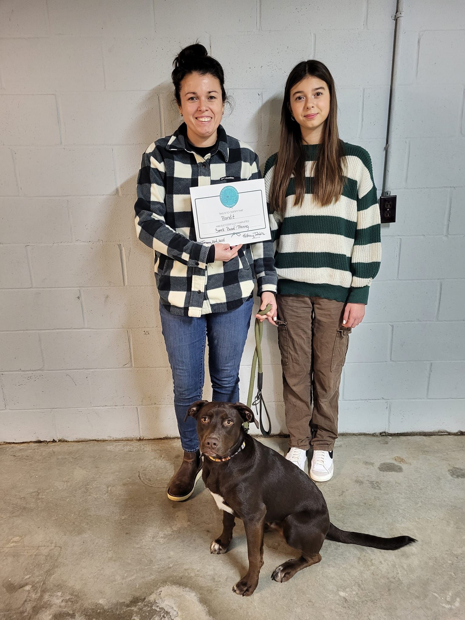 A woman and a girl are standing next to a dog and holding a certificate