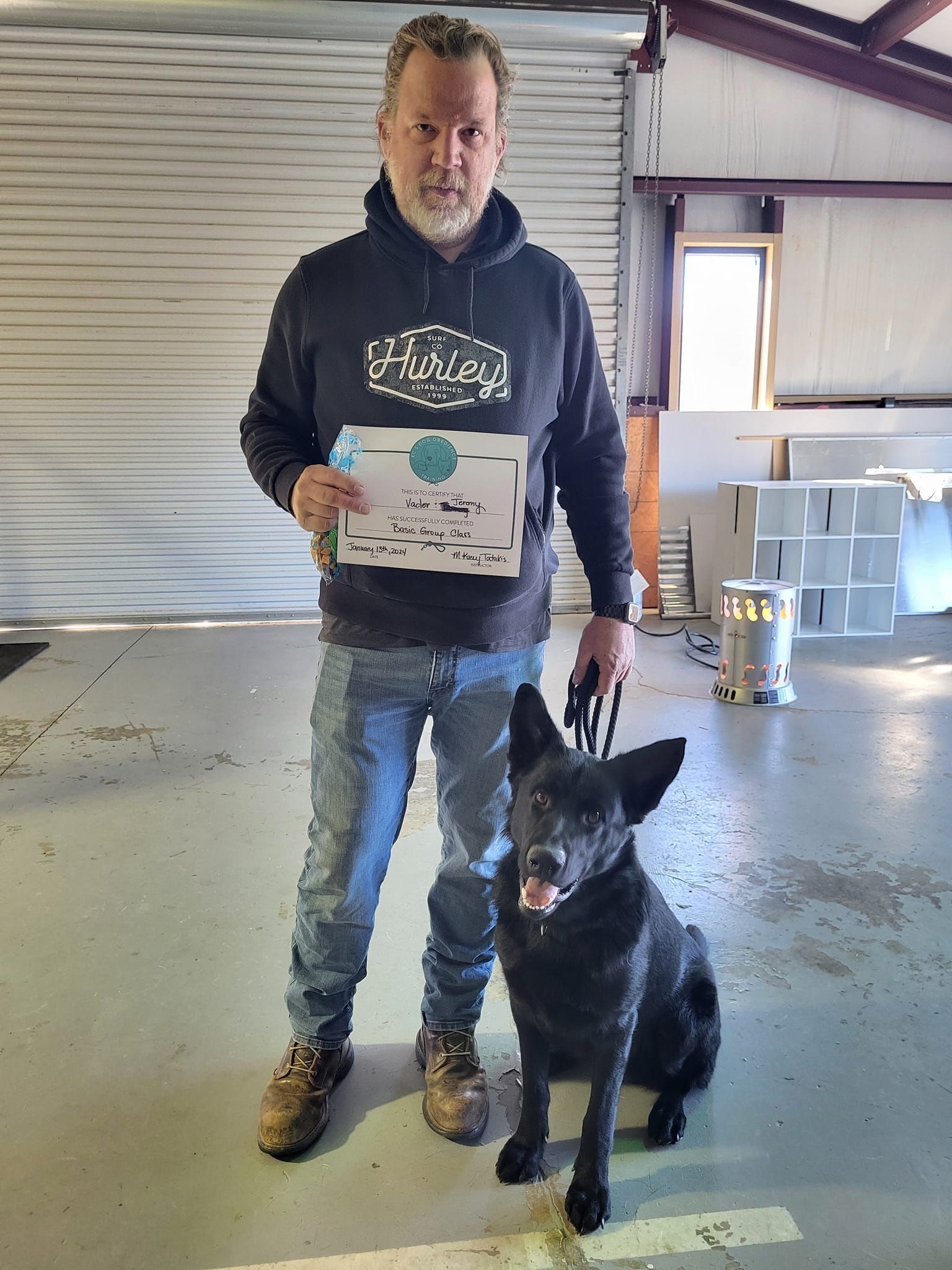 A man is standing next to a black dog and holding a certificate