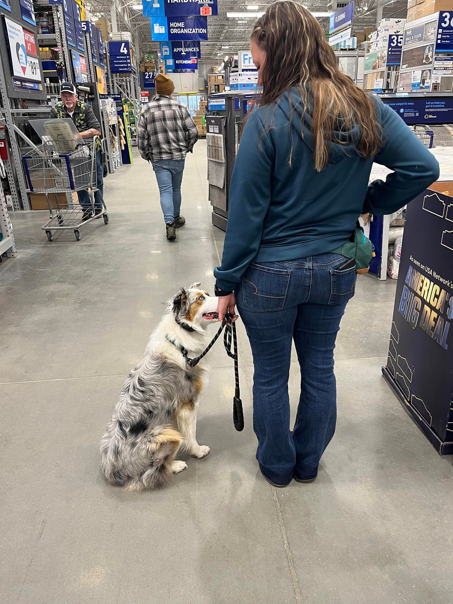 A woman is standing next to a dog on a leash in a store