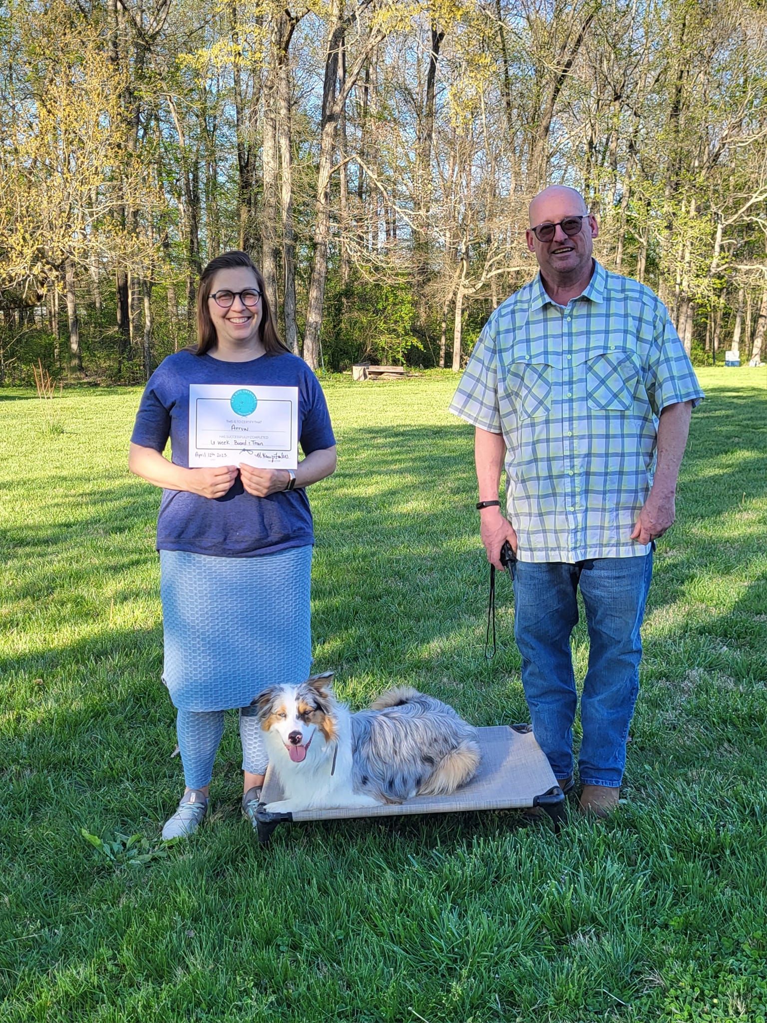A man and a woman are standing next to a dog in a field