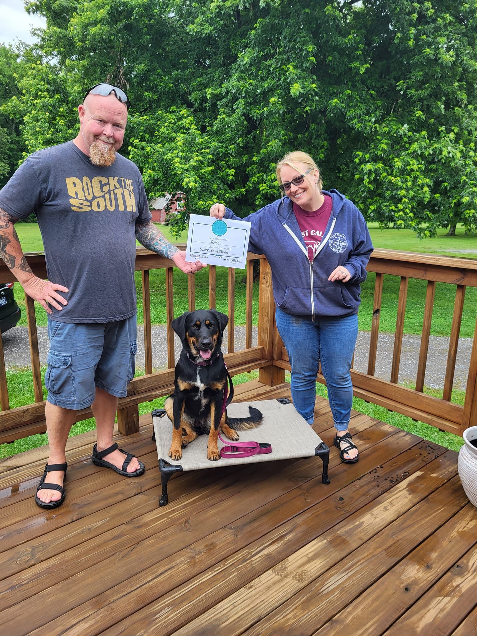A man and a woman are standing on a deck with a dog