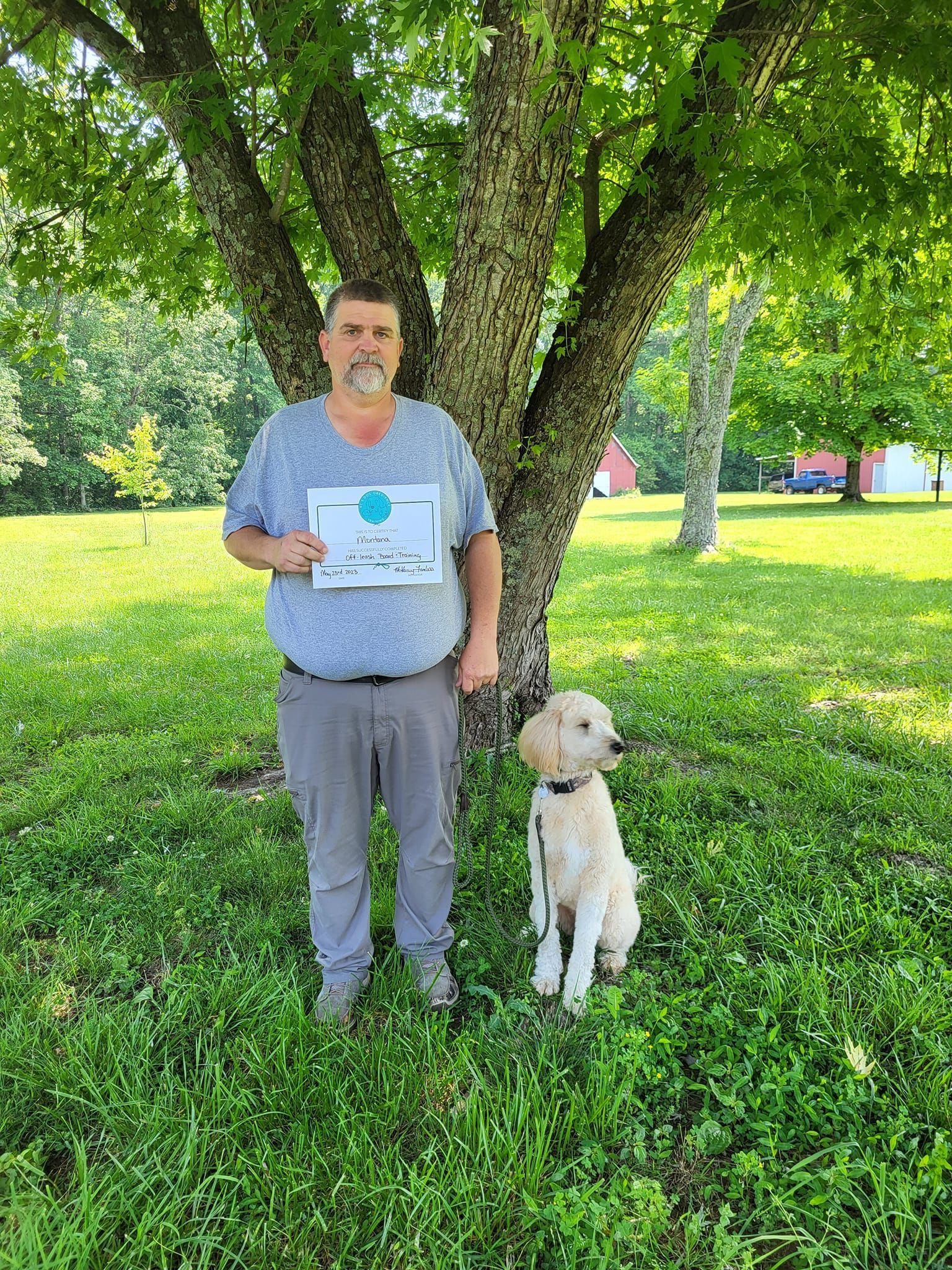A man is standing next to a dog in a park holding a sign