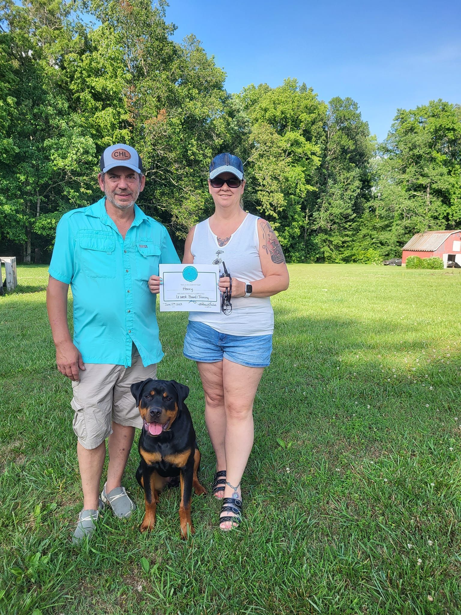 A man and a woman are standing next to a dog in a field holding a certificate