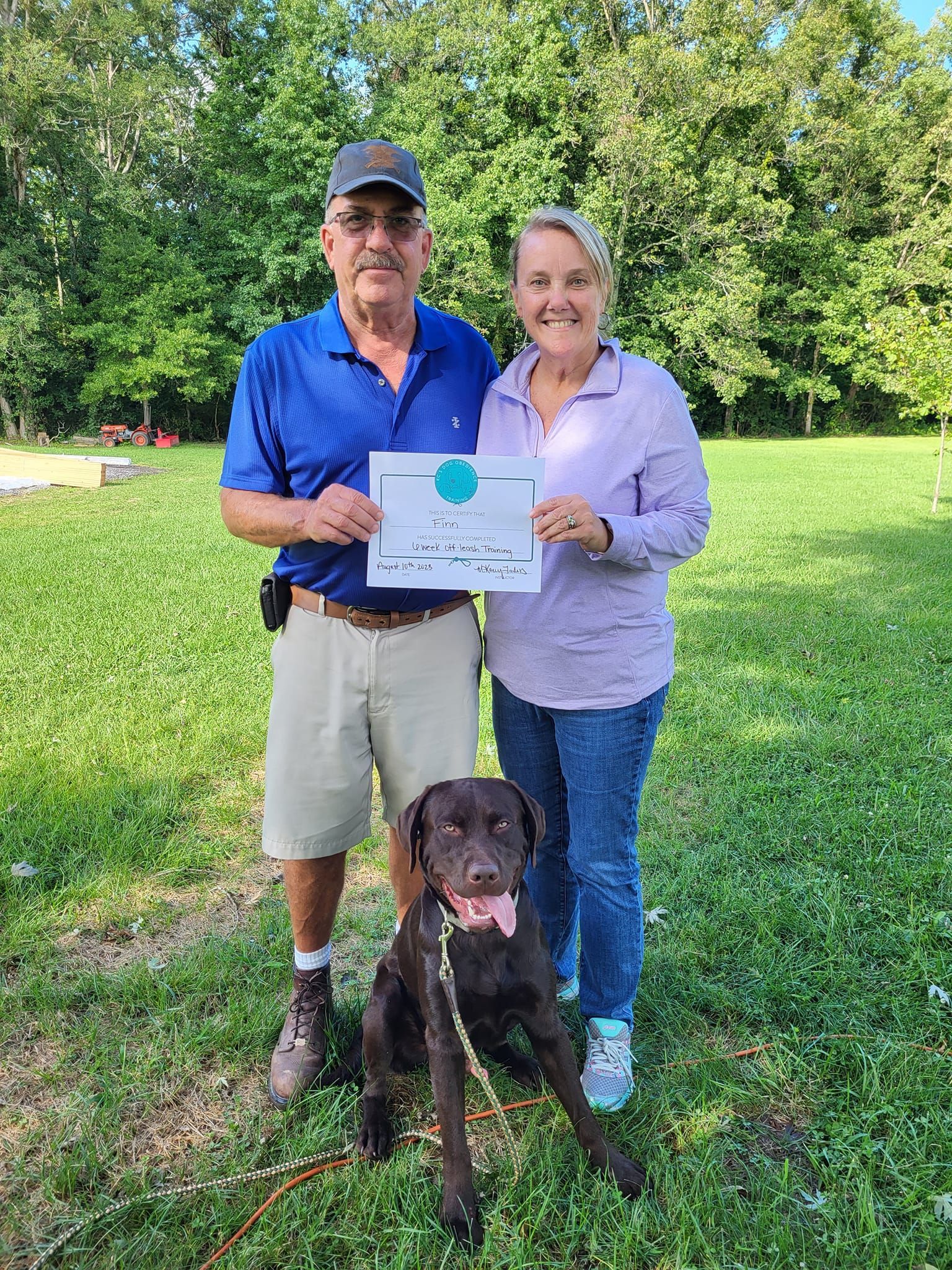 A man and a woman are standing next to a dog and holding a certificate