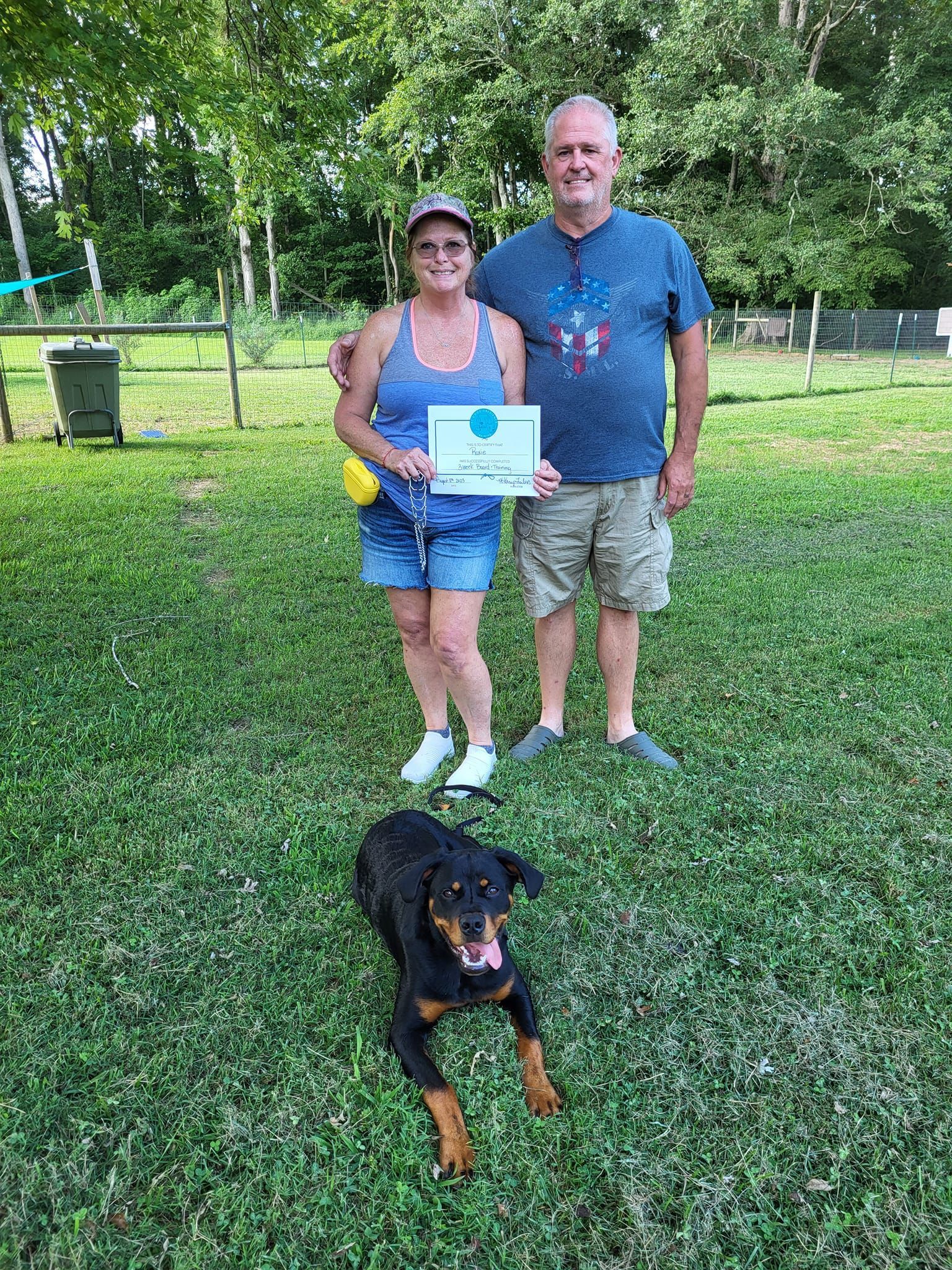 A man and a woman are standing in the grass with a dog