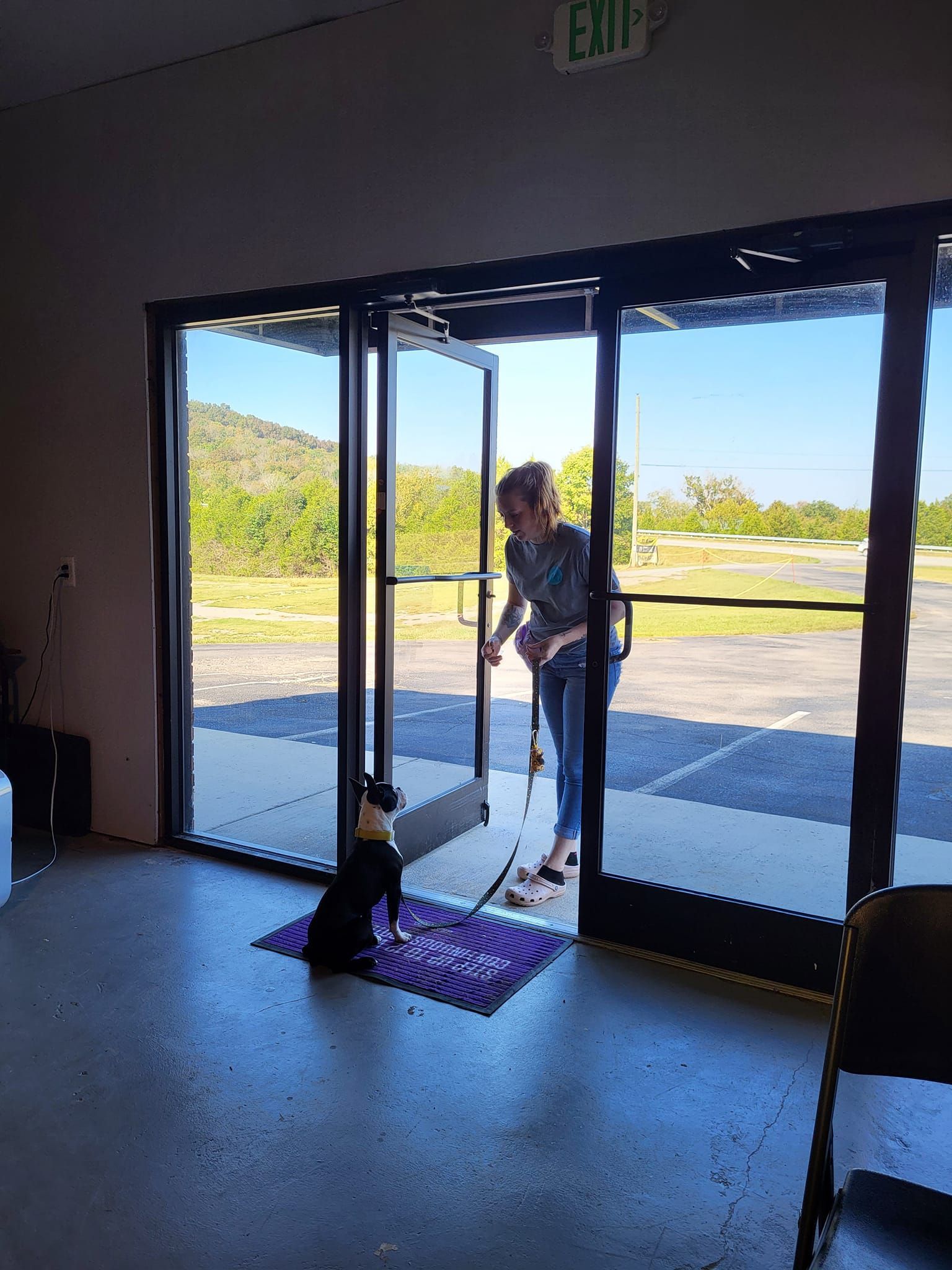 A woman is opening the door of a building with a dog sitting on the floor