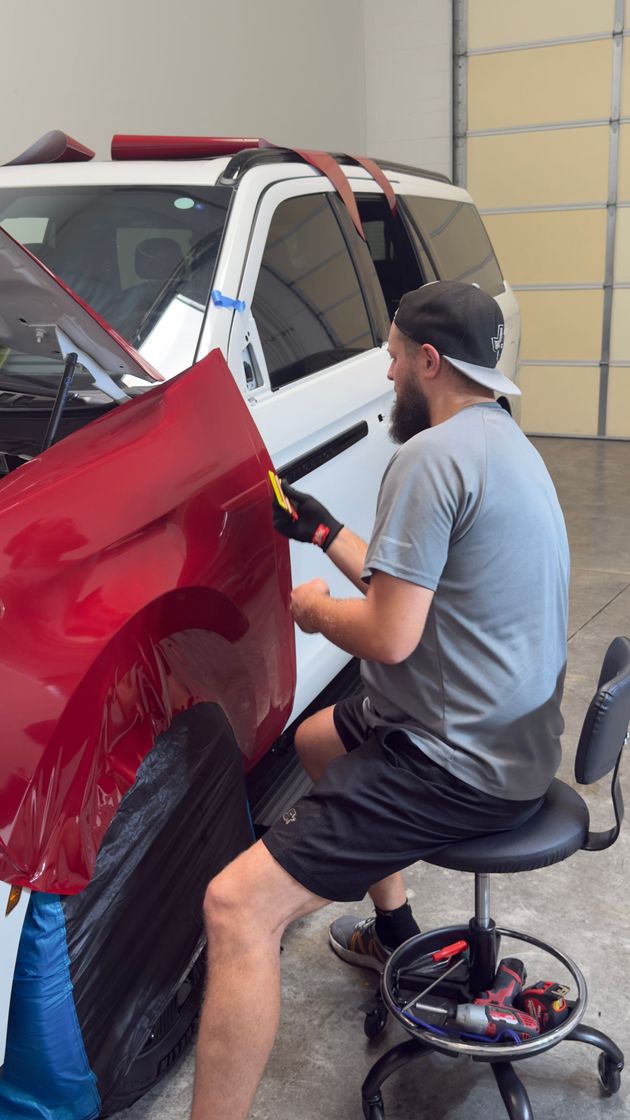 Mechanic polishing a red car door beside a white vehicle in a garage