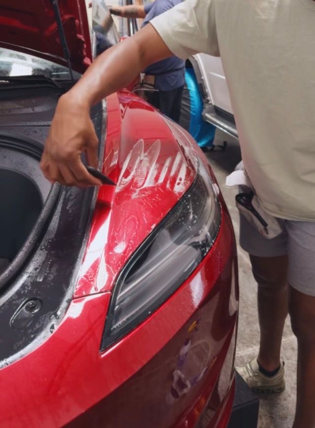 Person washing a red car’s rear with soapy water at a car wash