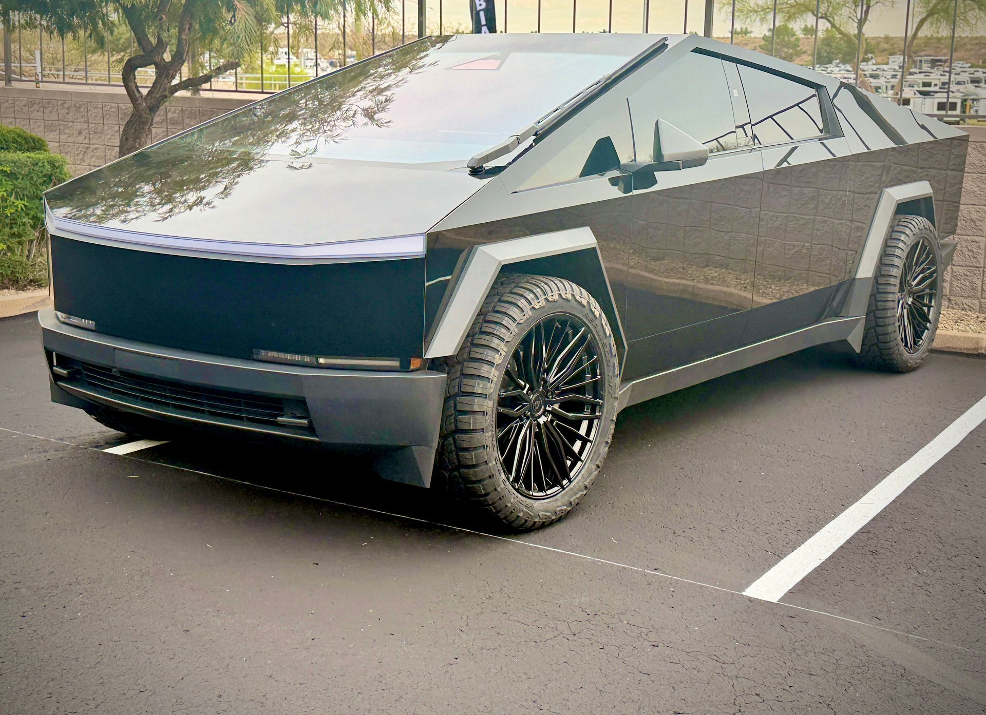 Silver Tesla Cybertruck parked on a road, angled front view under trees.
