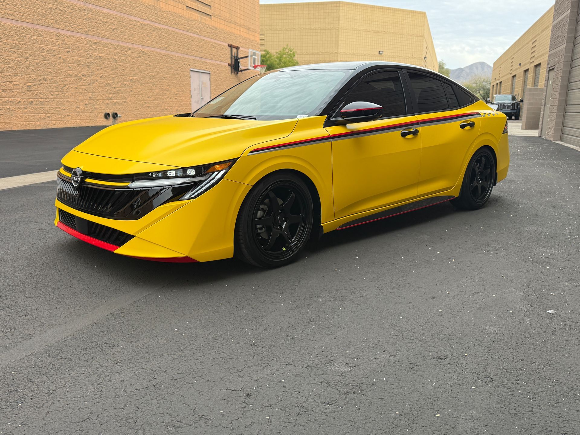 Yellow sports sedan with black roof and wheels parked in an alley between brick buildings
