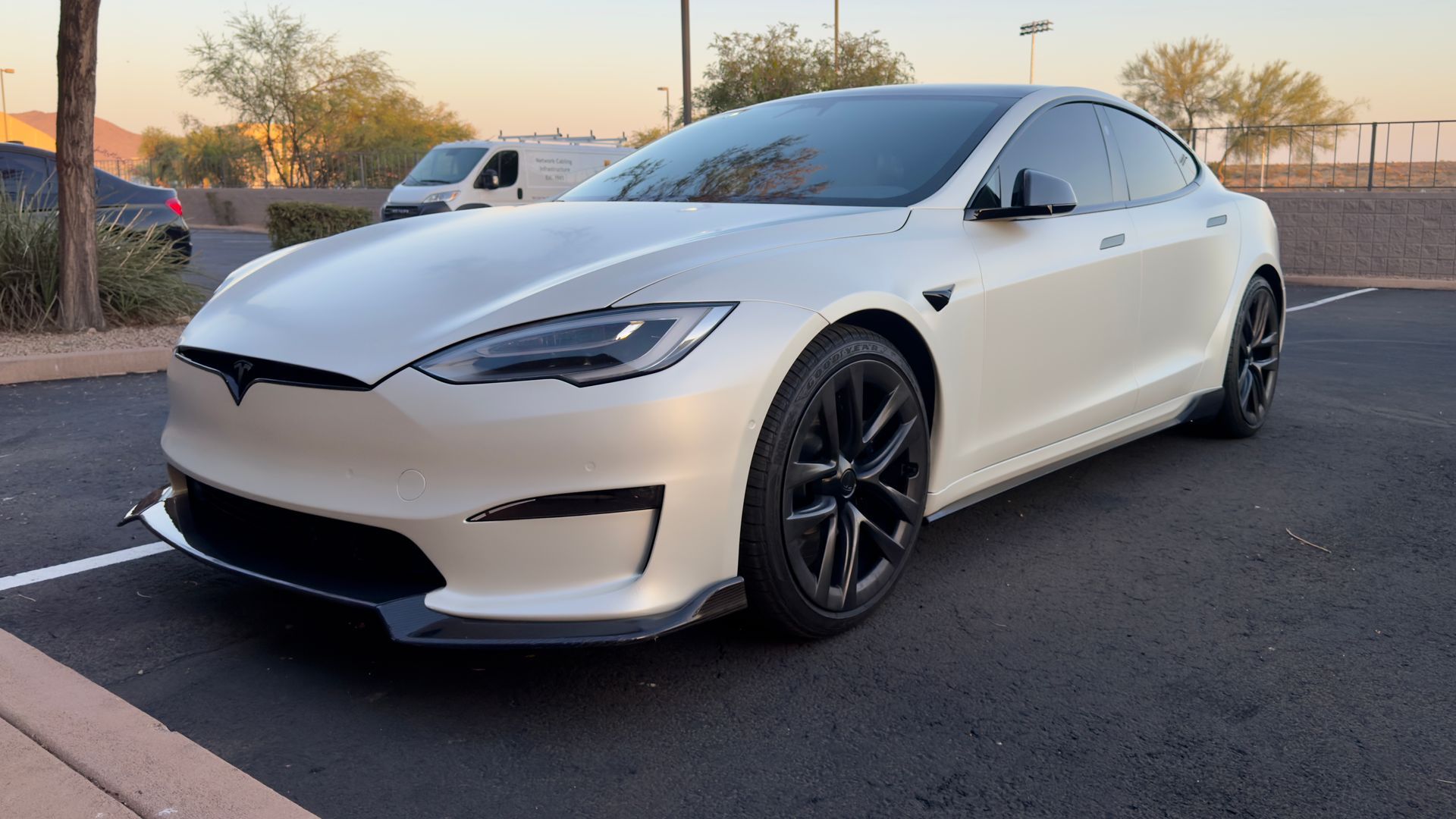 White Tesla sedan parked on a lot at sunset, front-left view with black wheels.