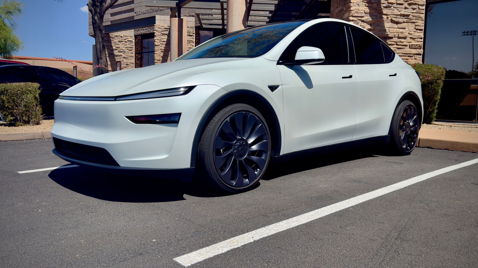 White Tesla Model 3 parked in a sunny driveway beside a stone house