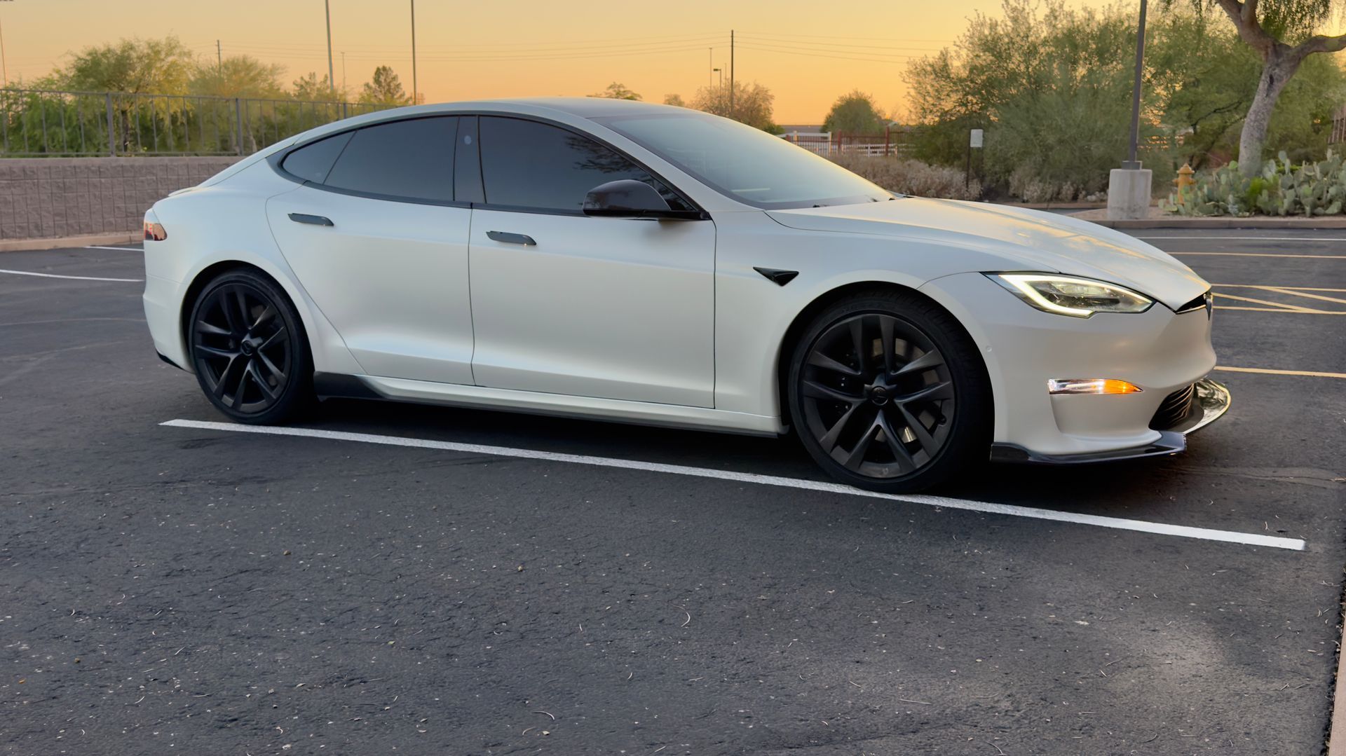 White Tesla sedan parked in a lot at sunset, with black wheels and tinted windows
