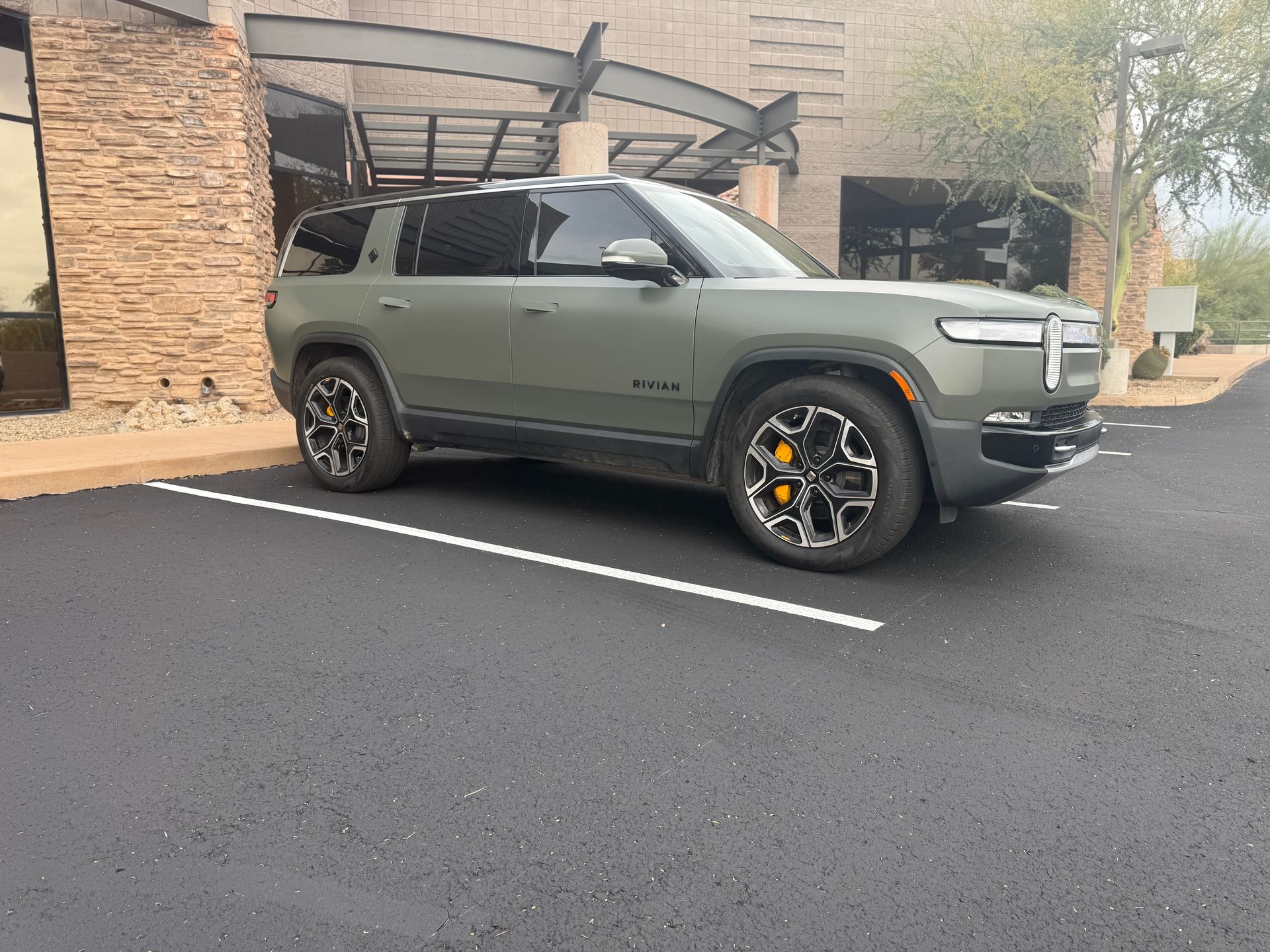 Olive green SUV parked in a lot beside a brick building, with black wheels and a roof rack.