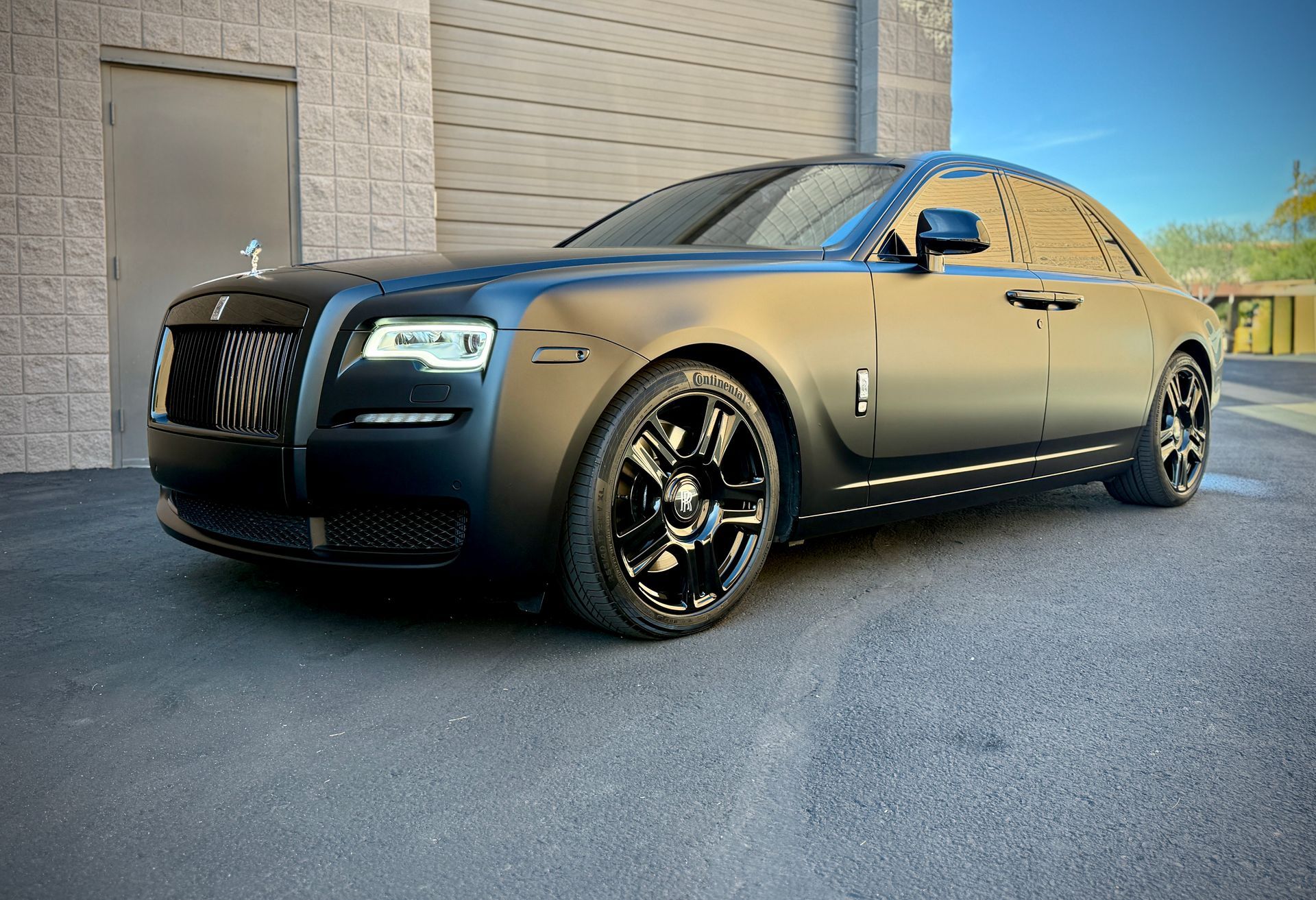 Black luxury sedan parked beside a building on a sunny day