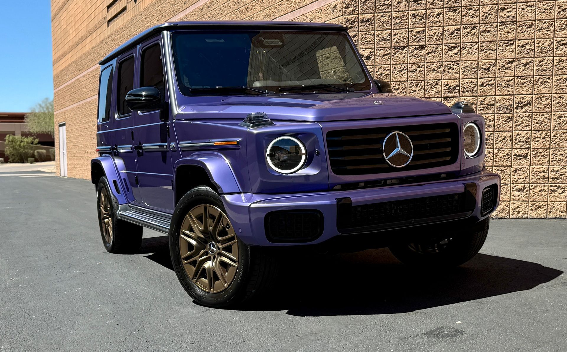 Purple Mercedes G-Wagon parked outside a brick building in bright sunlight
