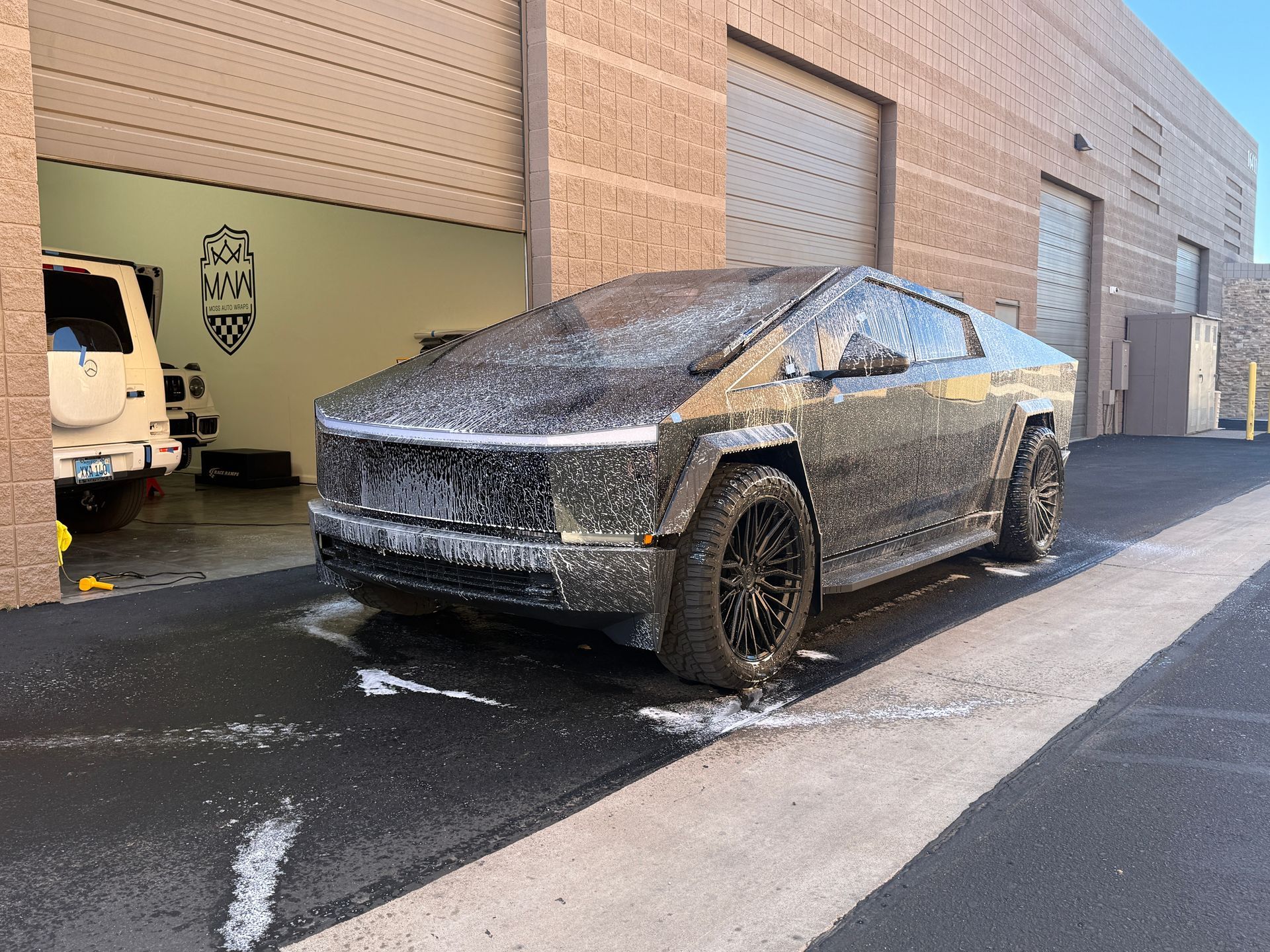Dust-covered Tesla Cybertruck parked beside a garage bay with a white van inside.