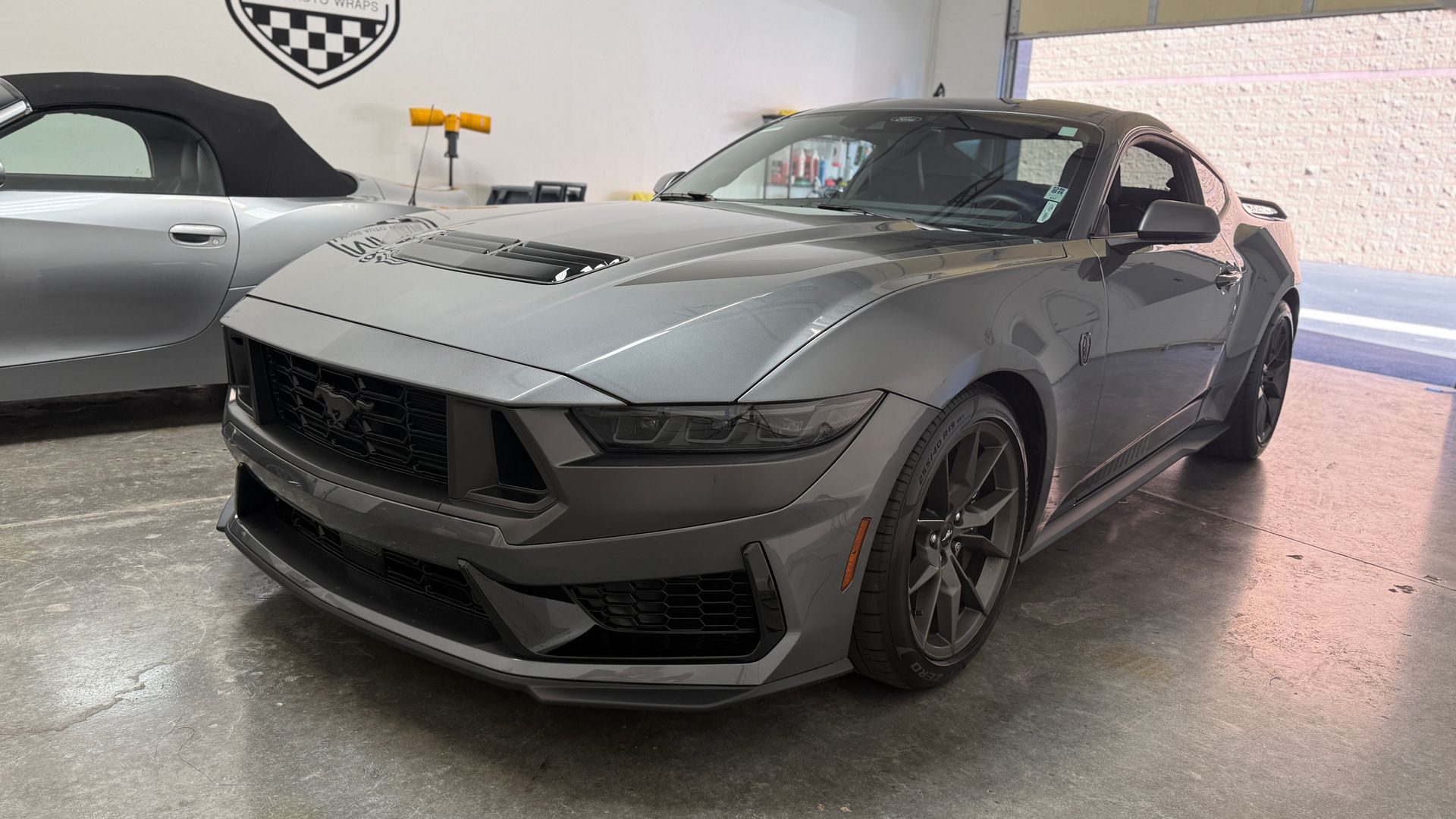 Gray sports car parked indoors in a showroom, front three-quarter view on a glossy floor